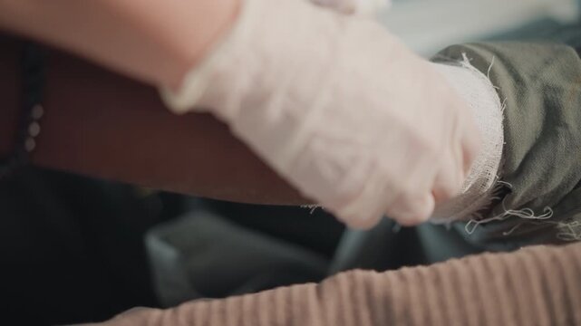 Emergency wound care. Medical aid for injury. Healthcare professional applying sterile bandage to patient indoors. Medical responder providing precise wound management using sterile supplies indoors