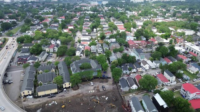 Neighborhood construction frame near curved corridor captures ongoing site work, machinery clusters, dense residential blocks extending toward peninsula core, mixed roof colors, Charleston, SC
