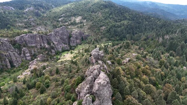 Aerial panoramic view of dramatic rock formations rising above a dense pine forest valley in Mineral del Chico, Hidalgo, Mexico, in a sunny day, 4K 60fs horizontal orbit drone shot