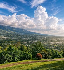 Obraz premium Lush green valley stretching beneath magnificent cloud formations and distant mountains. A breathtaking panorama celebrating nature, travel, and the beauty of open landscapes.