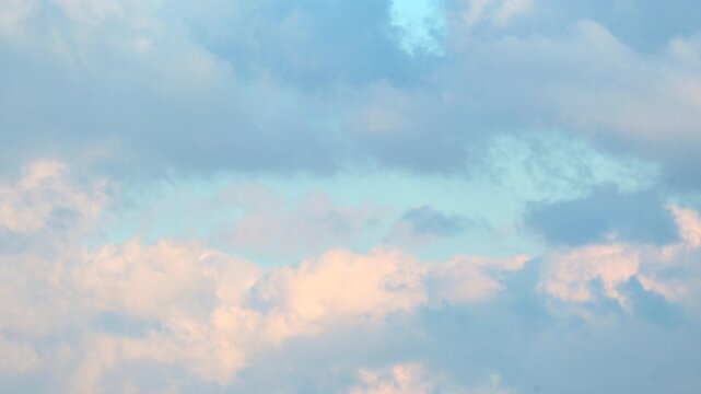 Layered white and pink cumulus clouds spread across a blue sky, captured at sunset with no landscape visible in the frame.