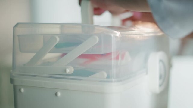 Closeup hands opening medical kit, white paramedic prepping supplies in home setting, clear plastic case with bandage and vial, soft natural light, calm focused motion, covidsafe routine
