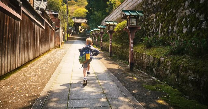 Slow motion shot of lone child with backpack running down alley of ancient Japanese village