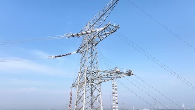 High voltage transmission tower with power lines against a clear blue sky background