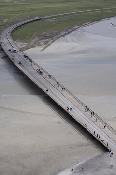 High angle view of tourists and pedestrians walking along the modern causeway bridge leading to Mont Saint-Michel in Normandy, France.