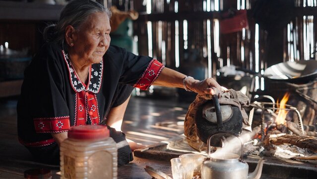Elderly woman pouring hot water from traditional kettle over open fire