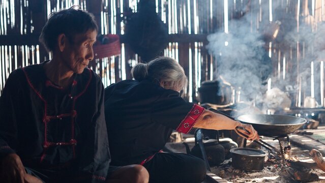 Elderly tribal couple preparing food over open fire in rustic home