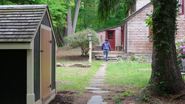 Man walking along backyard stone path to historic New England house 