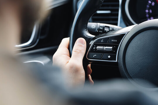 Driver hand holding modern car steering wheel. Vehicle interior closeup. Dashboard control buttons visible. Everyday travel and safe driving concept inside passenger car cabin and commute.