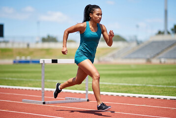 Obraz premium Athletic woman running and clearing hurdle on track field