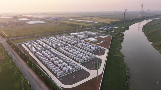 Aerial view of riverside energy storage power station with containerized battery units and industrial infrastructure