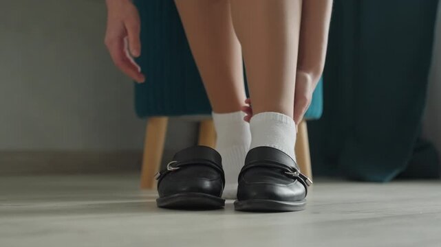 Woman at home removing shoes, then places loafers beside chair to keep house clean, white socks on laminate floor, calm morning atmosphere, gentle movements and tidy interior details