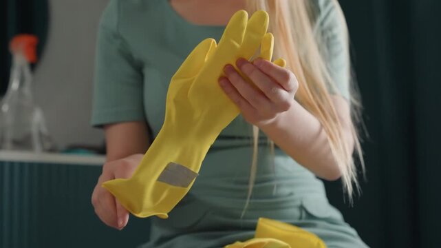 Woman washes gloves in gentle sunlight. Person squeezes water from gloves during quiet cleaning moment. Individual carefully wrings out water from yellow gloves in natural indoor lighting