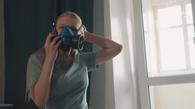 Caucasian technician secures respirator for cleaning. Professional restoration posture by window, adjusting straps and filters, checking seal and gear, preparing decontamination and remediation