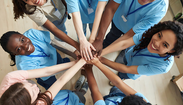 Diverse group of people in blue t-shirts with lanyards joining hands in a circle overhead shot, teamwork and unity