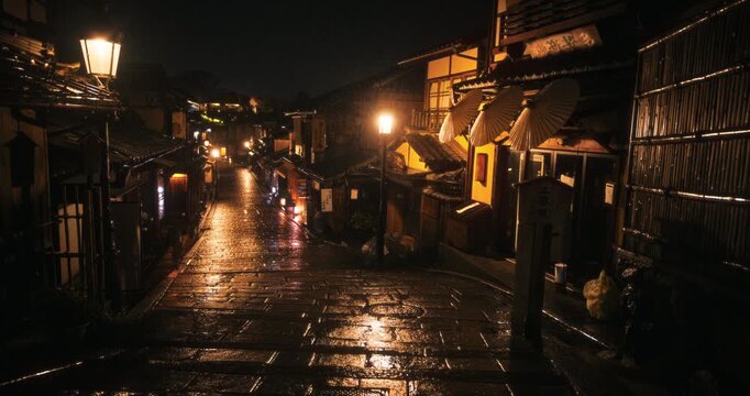 View down wet cobblestone slope through ancient Japanese town at night