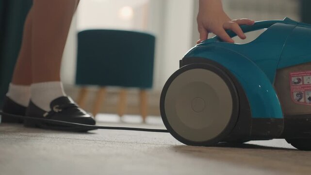Caucasian girl plugging vacuum cord, lowangle closeup of feet in socks and shoes beside turquoise canister, careful hand connecting plug to outlet, focus on safety, cord management and deliberate