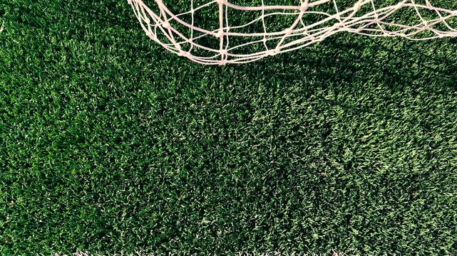 High-angle camera tilt down from a white soccer net to reveal a crisp, clean white goal line painted on a vibrant green artificial turf sports field.