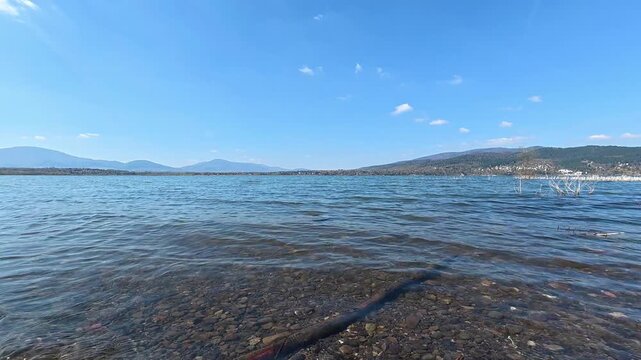 Mountain lake with gentle waves under blue sky. Natural water landscape with lake surface, distant mountains and clear weather. Nature background, travel destination, outdoor recreation