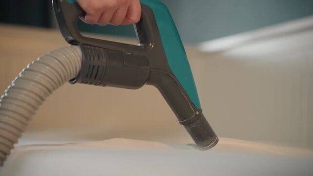 Professional mattress cleaning demonstration with nozzle, operator hand guiding handheld extractor across fabric, strong suction and hose movement lifting dust, modern bedroom background, efficient