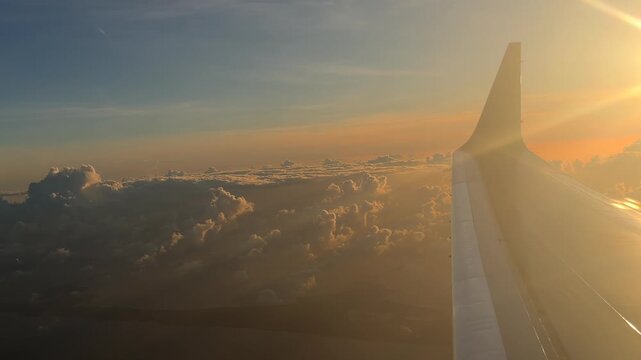 airplane wing flying through clouds at sunset