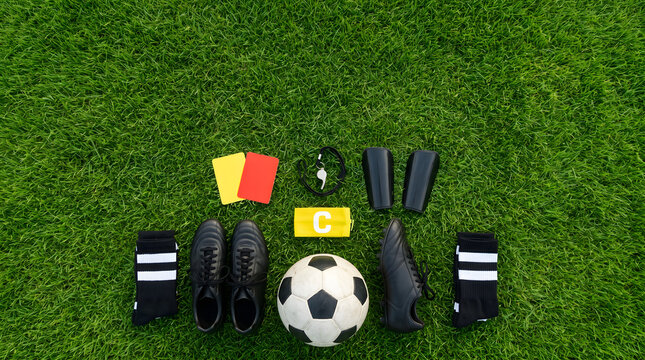 Soccer equipment neatly arranged on a green field, including a ball, cleats, socks, shin guards, and referee cards