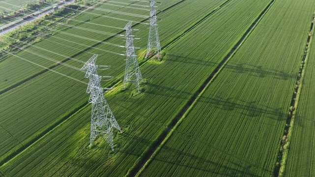 High voltage transmission towers and power lines over green agricultural fields