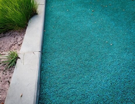 green playground rubber floor with concrete curb realistic photo of teal safety surfacing next to cracked concrete and weeds ideal for texture and urban background use