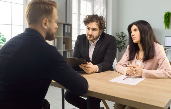 Interview recruiters with candidate in hiring discussion. Two managers evaluate a male applicant with resume in a bright office, focusing on fit. Theme is recruitment and hiring agreement.