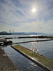 Fototapeta premium Coastal swimming pools with sun reflection and industrial background