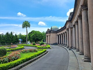 Fototapeta premium Curved stone colonnade with manicured flower gardens and palm tree