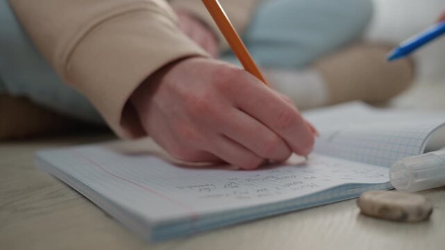 Close up hand writing grammar workbook in home tutoring session, pencil gliding over dotted pages, eraser beside notebook, tutor guiding student through spelling and sentence exercises, warm soft