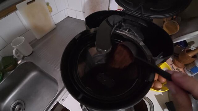 Slow motion close up of a person pouring ground coffee into a coffee maker filter to brew a fresh morning cup.