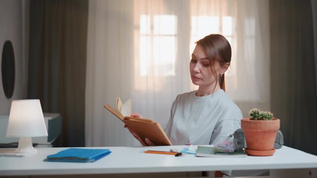 Caucasian tutor reading grammar book desk, soft sunlight through curtain, cozy workspace with lamp and succulent, woman flips pages while annotating sentences, practicing pronunciation