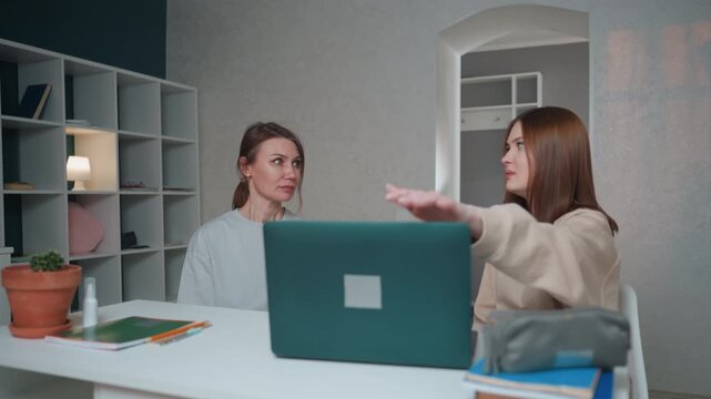 Caucasian tutor and student during critique session tutor delivers corrective feedback while student listens laptop closed on desk notes and textbooks visible tutor gestures emphatically student
