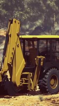 A large backhoe loader is parked at a construction site. The scene shows dust on the ground and greenery in the background. The sun is shining on the machinery.
