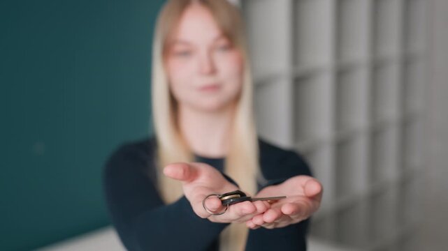 White woman offering open palm keys inside empty apartment with teal wall and shelving, tenant accepting new home keys, gentle smile, soft focus, moving and beginning of relocation