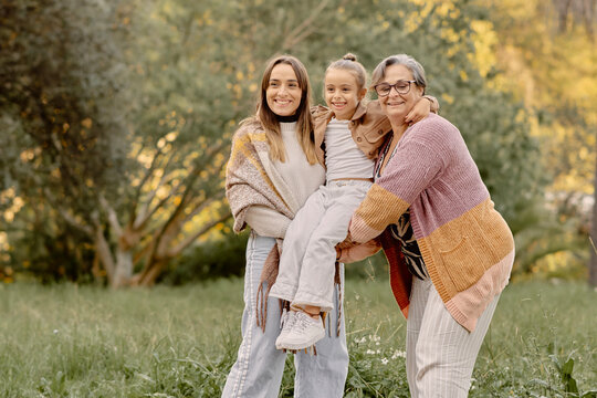 Multi generational family holding a child outdoors, captured in a full body shot from a low angle. Warm natural light, autumn tones and genuine
