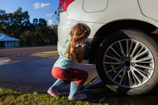 Young child helping wash family car parked on driveway in suburban front yard