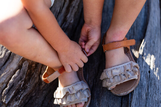 Child doing up buckles on sandal shoes while sitting on log outdoors