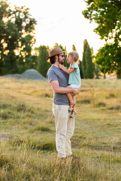 Aussie father holding young daughter together in grassy parkland reserve at sunset