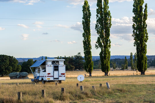 Camper trailer with satellite dish set up in paddock landscape