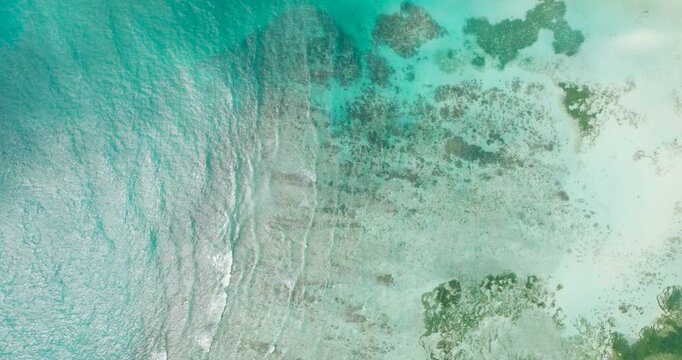 Emerald green ocean contrasts with the intricate shallow reef patterns, depicting a tranquil seascape. Seychelles, Mahe.
