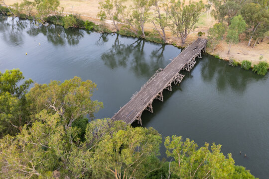 Aerial view of a derelict wooden bridge across an tree lined inland river