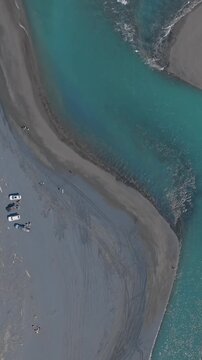 Aerial view of people with vehicles on the braided riverbed of the Marokopa River, in the Waitomo region of New Zealand. The turquoise water flows through the landscape.