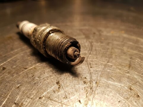 Worn Spark Plug Lying on Steel Workshop Surface with Damaged Electrode End Visible