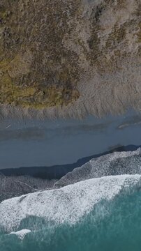 Aerial view of the coastline where the turquoise ocean meets the black sand beach in Marokopa, New Zealand. The waves crash against the shore. Scenic landscape.