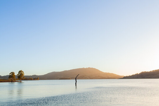 Sun setting across still scene of calm inland lake waters with sun dipping below horizon