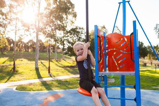 Happy little girl playing outdoors swinging on flying fox zipline at park playground