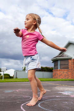 Child running about outdoors over chalk drawings on driveway